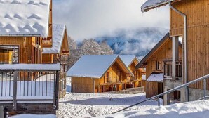 A wooden chalet-style building with a snow-covered roof and a view of mountains in the background. - Duplex Alpin de Charme | 2 Ch. • Jusqu'à 8 pers. (La Féclaz)