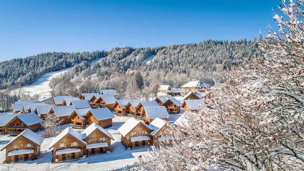 A cluster of wooden cabins with snow-covered roofs, set against a backdrop of a snow-covered forest and a clear blue sky. - Duplex Alpin de Charme | 2 Ch. • Jusqu'à 8 pers. (La Féclaz)