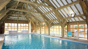 Una piscina interior con un alto techo de madera y grandes ventanales.