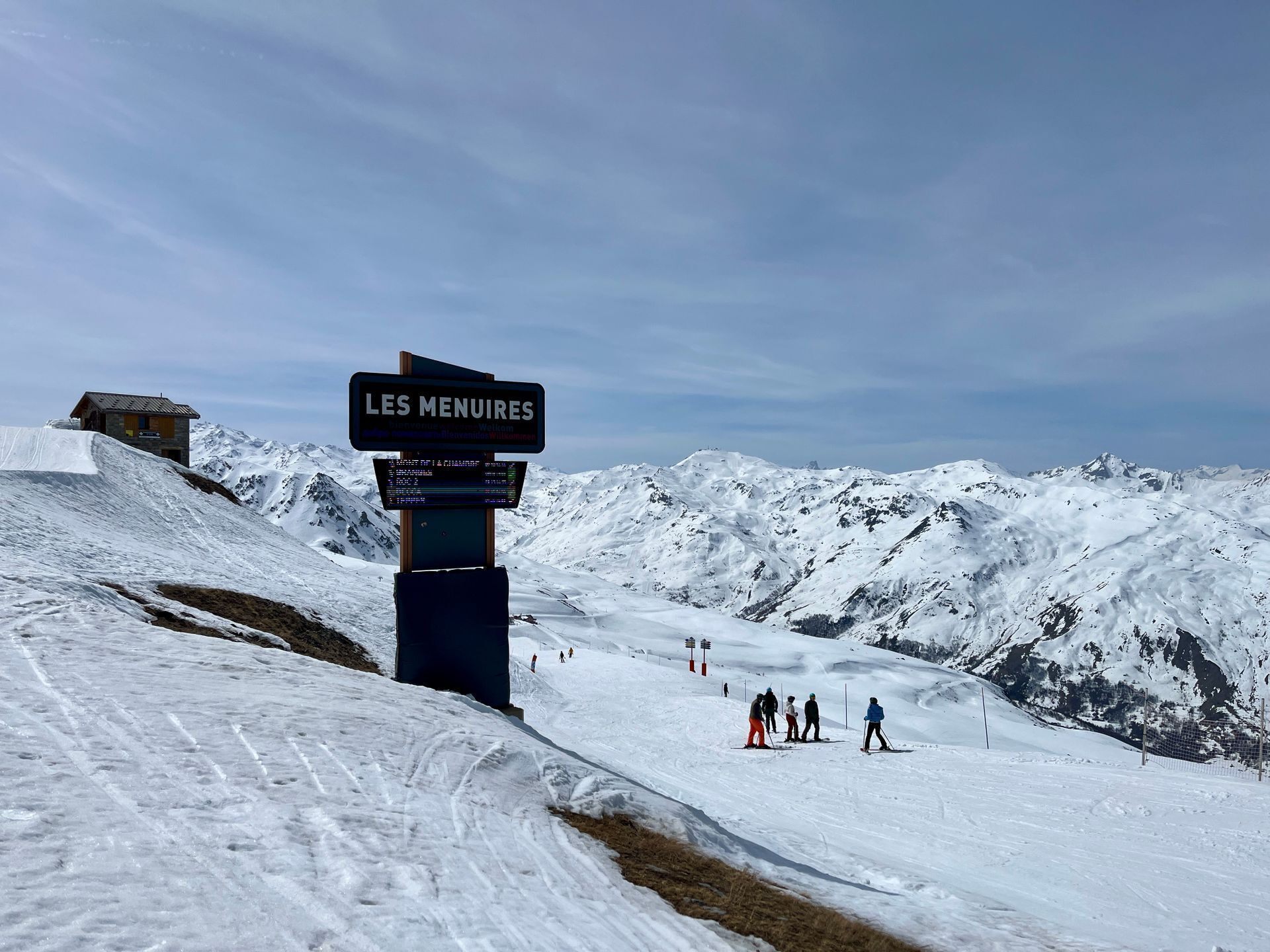 A signpost with 'LES MENUIRES' text, a ski slope, and a mountain backdrop.
