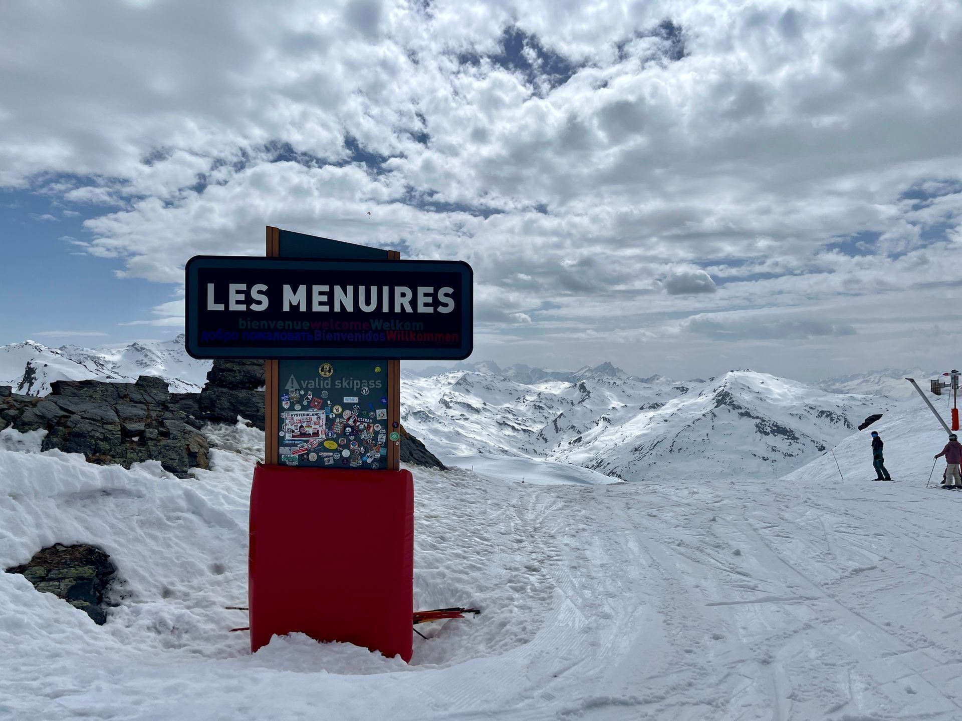 A sign with 'LES MENUIRES' welcoming visitors, a red structure, and a snowy mountain landscape.