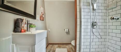 Een badkamer met een douche, wastafel en spiegel.