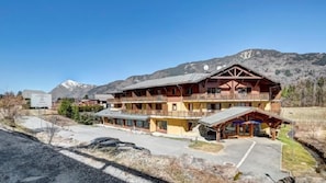 A multi-story wooden building with balconies, a covered outdoor area, and a mountainous backdrop.