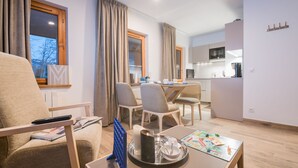A modern living room with a sofa, a dining table with chairs, a kitchen area with a microwave, and a window with curtains. - Praz-sur-Arly | Sleeps 4 | Family-Friendly Getaway (Praz-sur-Arly)