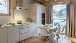 A modern kitchen with white cabinets, a stainless steel range hood, and a dining area with a table set for four. - Praz-sur-Arly | Sleeps 6 | Never-Ending Thrills (Praz-sur-Arly)