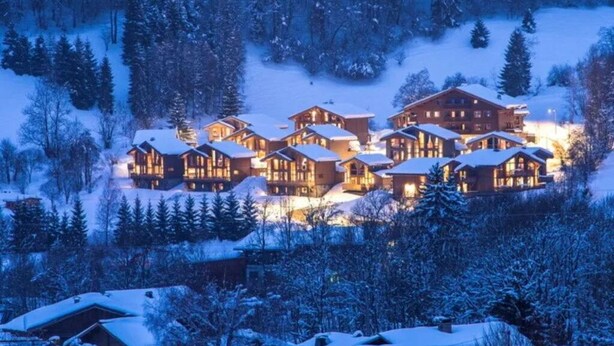 A snow-covered lodge with multiple wooden cabins, surrounded by trees and a snowy landscape. - Praz-sur-Arly | Sleeps 8 | Boundless Excitement (Praz-sur-Arly)