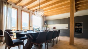 Una cocina moderna con armarios oscuros, techo de madera y una amplia mesa de comedor con sillas.