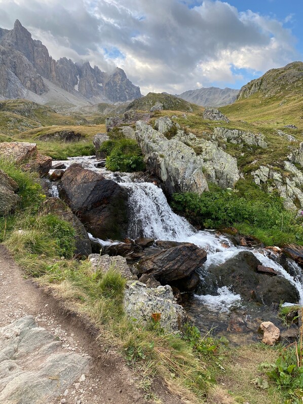 Paesaggio montuoso con un ruscello, terreno roccioso e cielo sereno.