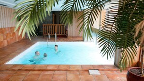Piscina interior com chão em azulejo, deck de madeira e parede de pedra.