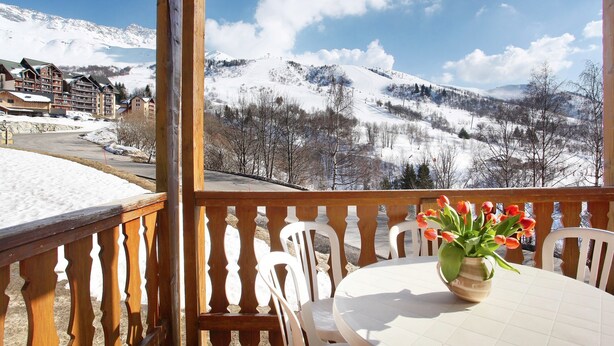 A balcony with a table and chairs, a vase with flowers, and a snowy mountain view.