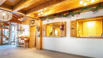 L’intérieur est en bois, avec un plafond haut, des poutres apparentes et un sol carrelé. On y trouve des fenêtres avec des volets en bois, un luminaire suspendu et un élément décoratif fixé au mur.