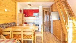 A wooden interior with a dining table and chairs, a kitchen with red cabinets, and a wooden staircase. - Sleeps 7! 2BR Apt| Scenic Living in Valmorel! (La Léchère)