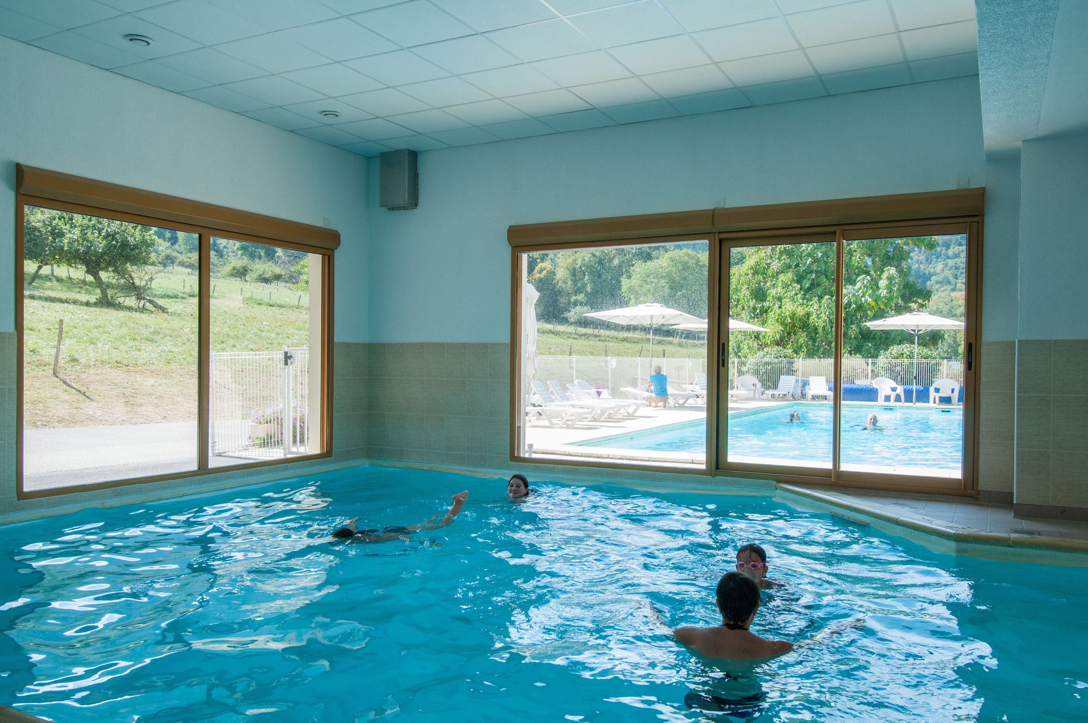 Piscina interna com grandes janelas, teto azulejado e vista para área de piscina externa.