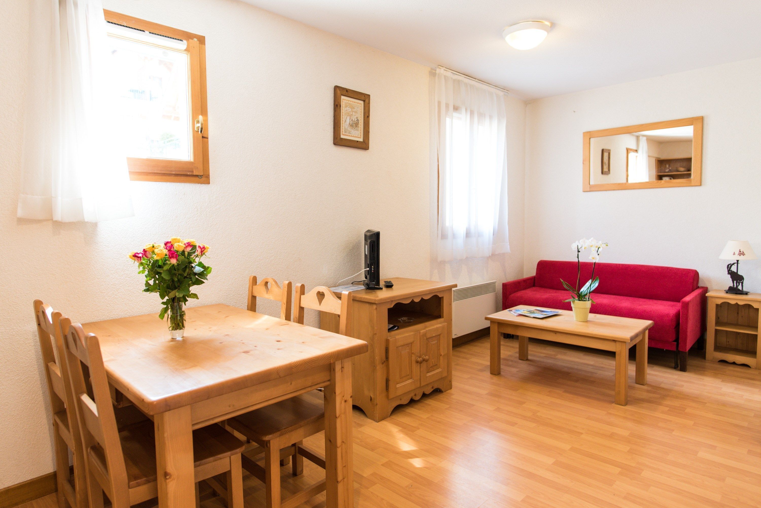 A cozy living room with a wooden dining table, chairs, a red sofa, and a small coffee table.