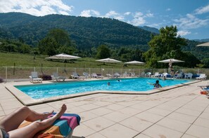 A swimming pool with lounge chairs and umbrellas, surrounded by a fence, with mountains in the background.