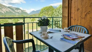 A balcony with a table set for two, a potted plant, a cup, a spoon, and a magazine.
