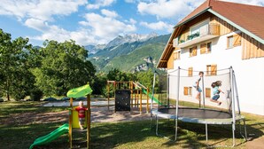 A playground with a slide and climbing wall, a trampoline, and a building with a balcony in the background.