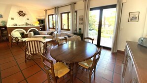 A spacious living area with a round wooden table and chairs, a sofa set, and a kitchen area with a stove. - Maison Familiale Proche Plage (PYLA SUR MER)