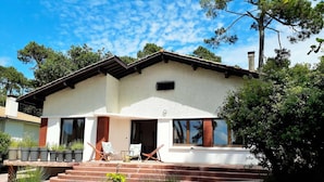 A two-story house with a patio area, a chimney, and a small garden. - Maison Familiale Proche Plage (PYLA SUR MER)