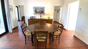 A dining area with a round wooden table surrounded by six chairs, a wooden cabinet with a radio, and a painting on the wall. - Maison Familiale Proche Plage (PYLA SUR MER)