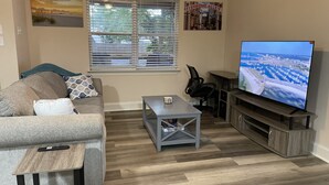 En stue med sofa, sofabord, fjernsyn og et vindue med persienner.