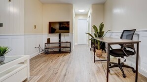 A modern, well-lit room with a wooden floor, a dining table with chairs, a TV mounted on the wall, and a potted plant. - Premier League Pad - with Free Parking, Heat & AC (Manchester)