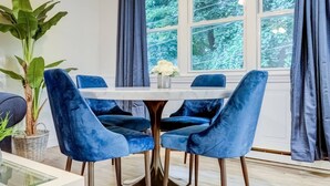 A dining area with a round table and four blue velvet chairs. There is a large potted plant on the left and a vase with white flowers on the table. - Premier League Pad - with Free Parking, Heat & AC (Manchester)