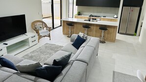 A modern living room with a grey sofa, a flat-screen TV, and a wicker chair. - New 5 Bedroom Home 1km from the Beautiful Busselton Beaches  (Geographe)