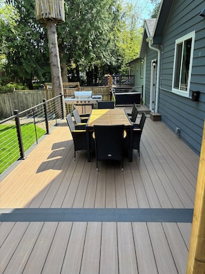 Una terraza de madera con mesa y sillas, una parrilla y un patio cercado.