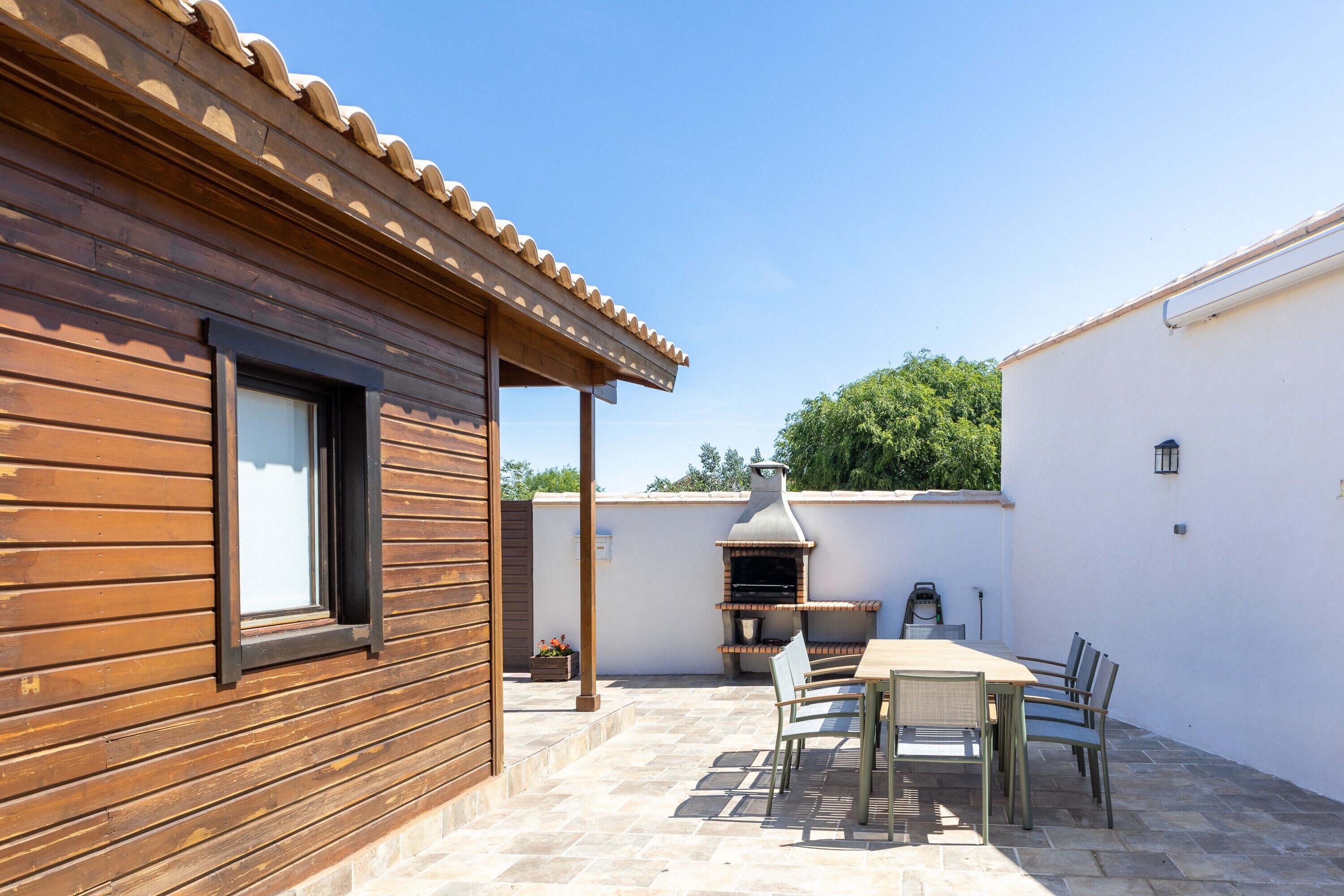 Una construcción de madera con un patio empedrado, una parrilla y una mesa con sillas.