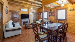 A wooden cabin interior with a living room, dining area, fireplace, and large windows. - Rural House 'La Dehesa2' in Toledo with Private Pool, Wi-Fi, and Air Conditioning (Cobisa)