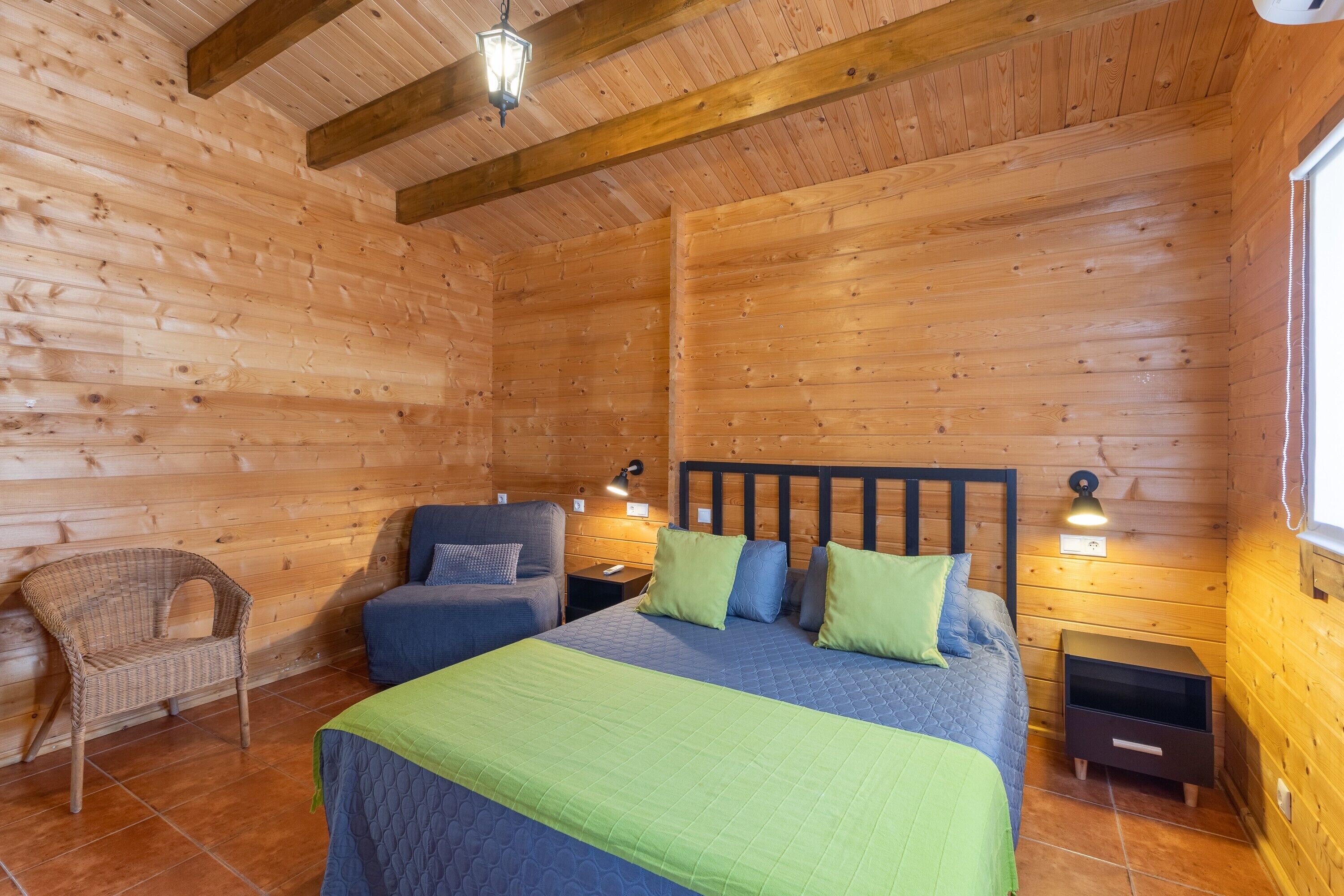 Habitación de cabaña de madera con una cama, dos sillas, una mesita de noche y una lámpara.