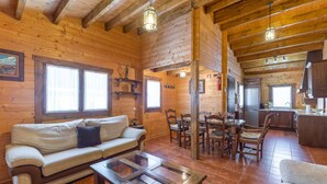 A wooden cabin interior with a sofa, dining table, chairs, and a kitchen area. - Rural House 'La Dehesa2' in Toledo with Private Pool, Wi-Fi, and Air Conditioning (Cobisa)