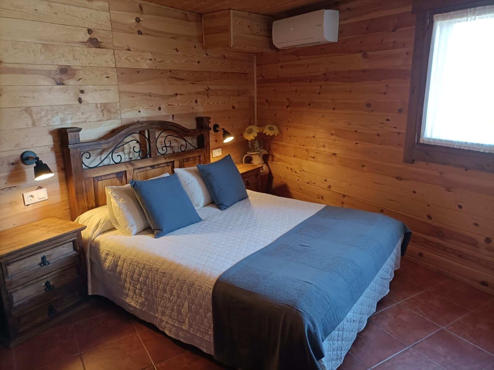 Habitación con paneles de madera, una cama, mesitas de noche, aire acondicionado instalado en la pared y una ventana.