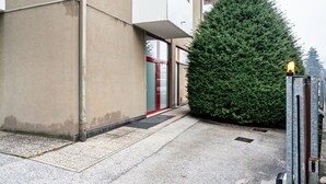A building entrance with a red door, a large evergreen tree, and a metal gate. - Apartment 'Trento Degasperi 16' with Wi-Fi (Trento)