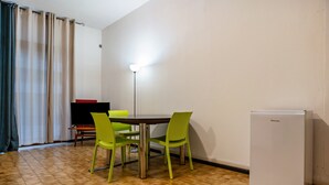 A small room with a dining table, two chairs, a refrigerator, a bench, and a floor lamp. - Apartment 'Trento Degasperi 16' with Wi-Fi (Trento)
