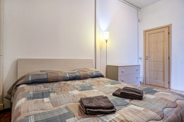 Ein Schlafzimmer mit Bett, Nachttisch, Lampe und Kleiderschrank.