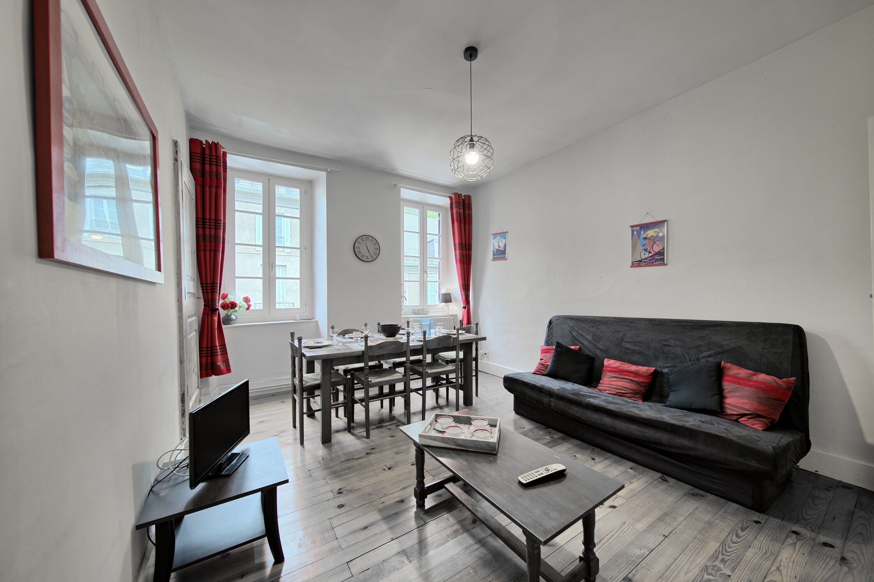 A living room with a sofa, a coffee table, a TV, a dining table with chairs, and a kitchen area.