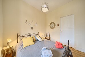 Et soveværelse med seng, sengeborde, lampe, stol, dør og billeder på væggen.