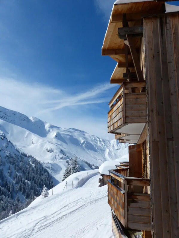 Un chalet en bois doté d’un balcon donnant sur un paysage montagneux enneigé.