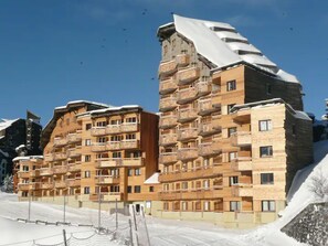 Ett hotell med flera våningar och balkonger, en skidbacke i bakgrunden och snö på taket.