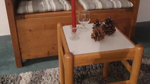 A wooden bench with two plush toys, a candle, a glass, and a pine cone on a small table.