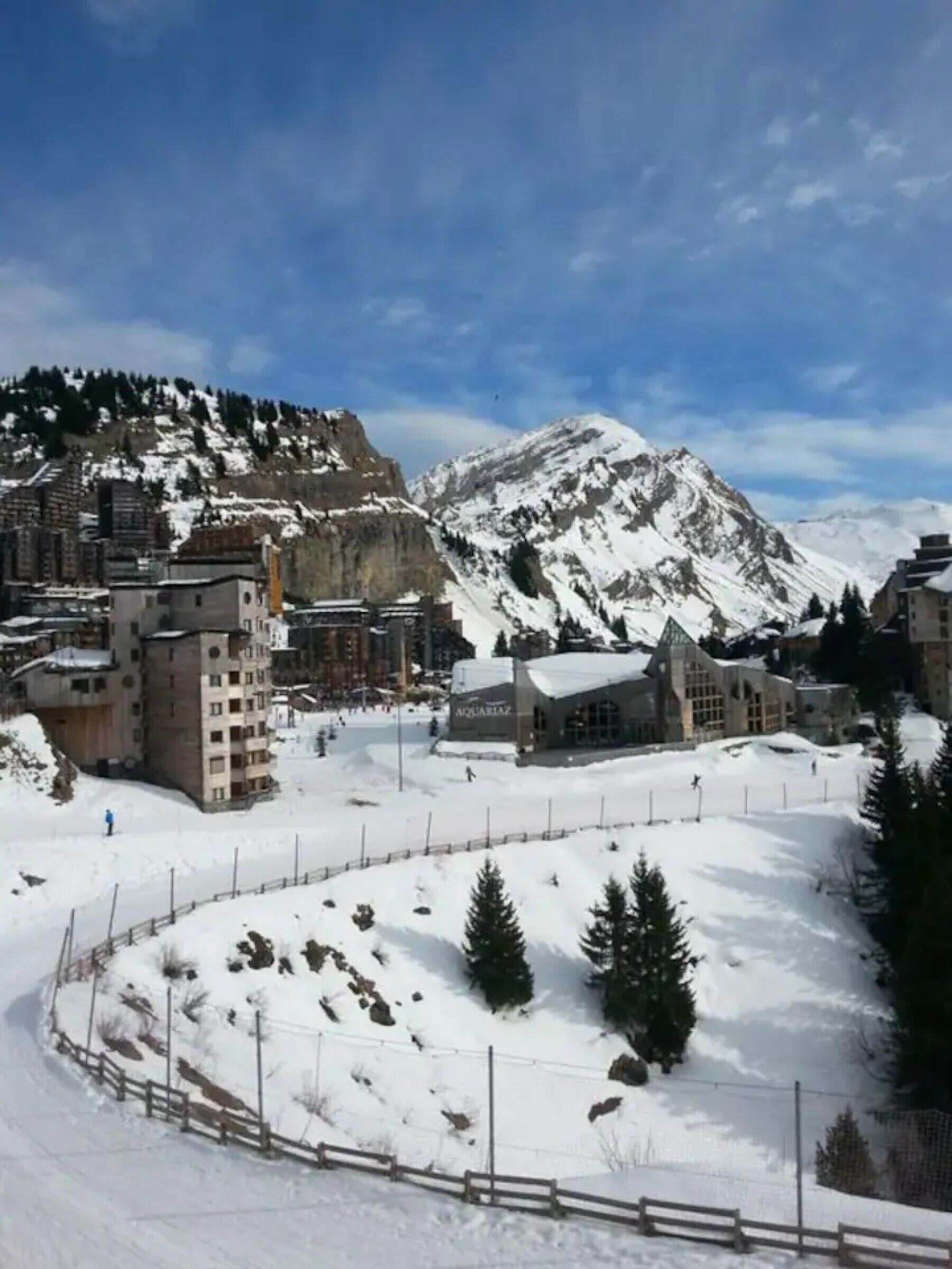 Une ville de montagne enneigée, avec des bâtiments, une zone délimitée par une clôture et un bâtiment remarquable portant l’inscription « AQUARIAZ ».