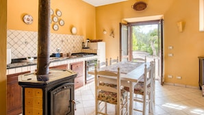 A kitchen with a stove, dining table, chairs, and a view through an open door. - Agriturismo "Il Grappolo E La Rosa - Sagrantino" with Shared Pool, Private Terrace, and Wi-Fi (Montefalco)