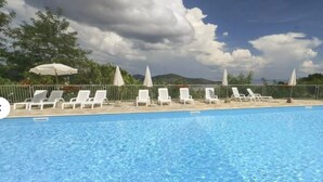 A swimming pool with white lounge chairs and umbrellas, surrounded by a fence and trees.