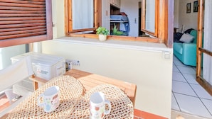 A room with a wooden-framed window, a table with a woven mat, and a view into another room with a sofa.