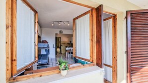 A room with a wooden-framed window, a small plant on the windowsill, and a view into a kitchen area.