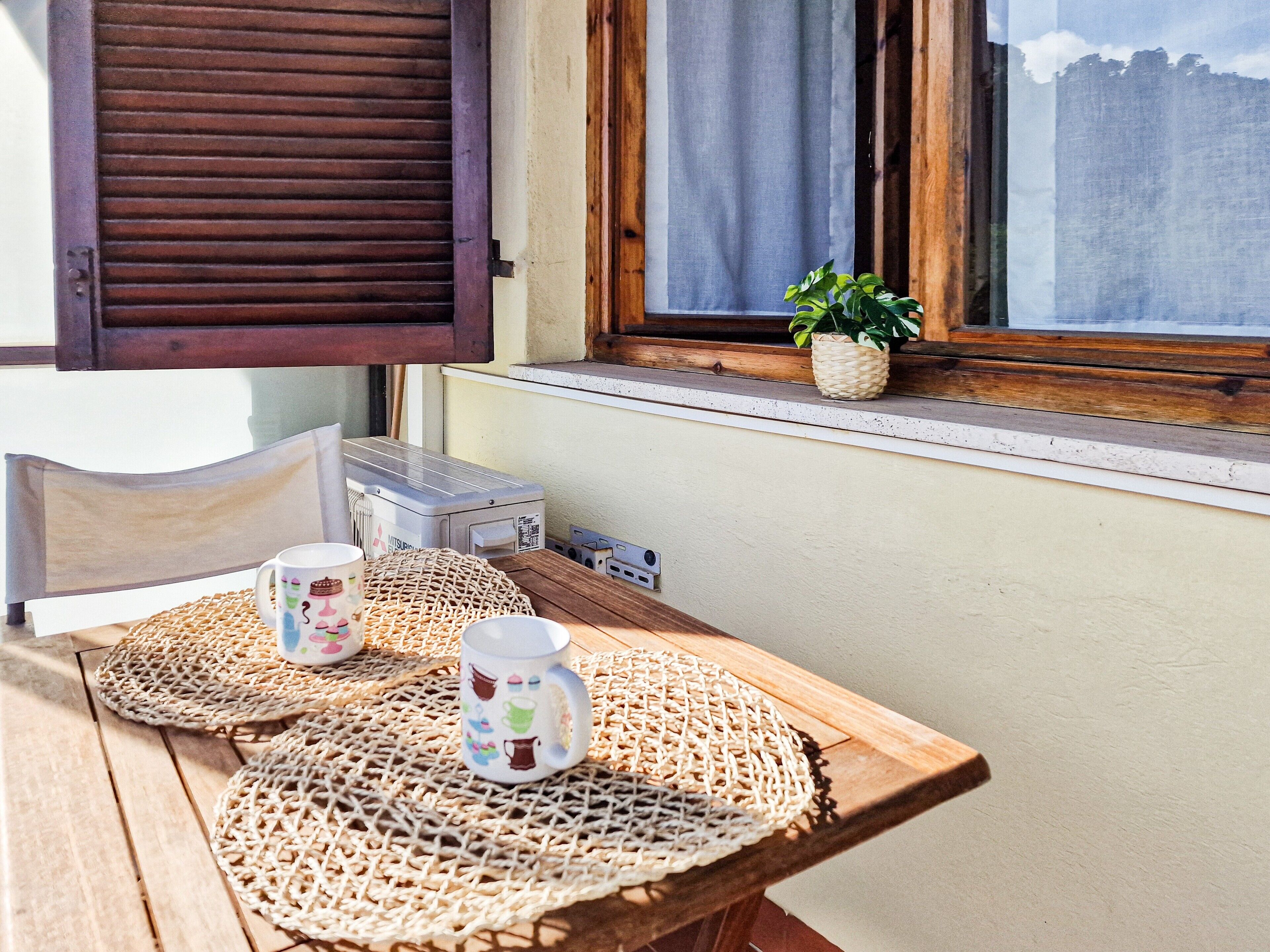 Ein Holztisch mit gewebten Tischsets, zwei dekorative Tassen, ein kleiner Topfpflanze und ein Fenster mit Holzhörnern.