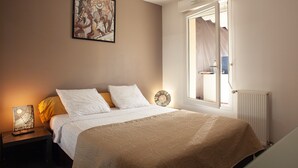 Un dormitorio con una cama, una mesita de noche con lámpara, una ventana con cortinas y una obra de arte colgada en la pared.