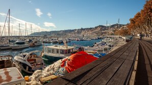 Un puerto deportivo con barcos amarrados, un muelle de madera y un paisaje montañoso al fondo.
